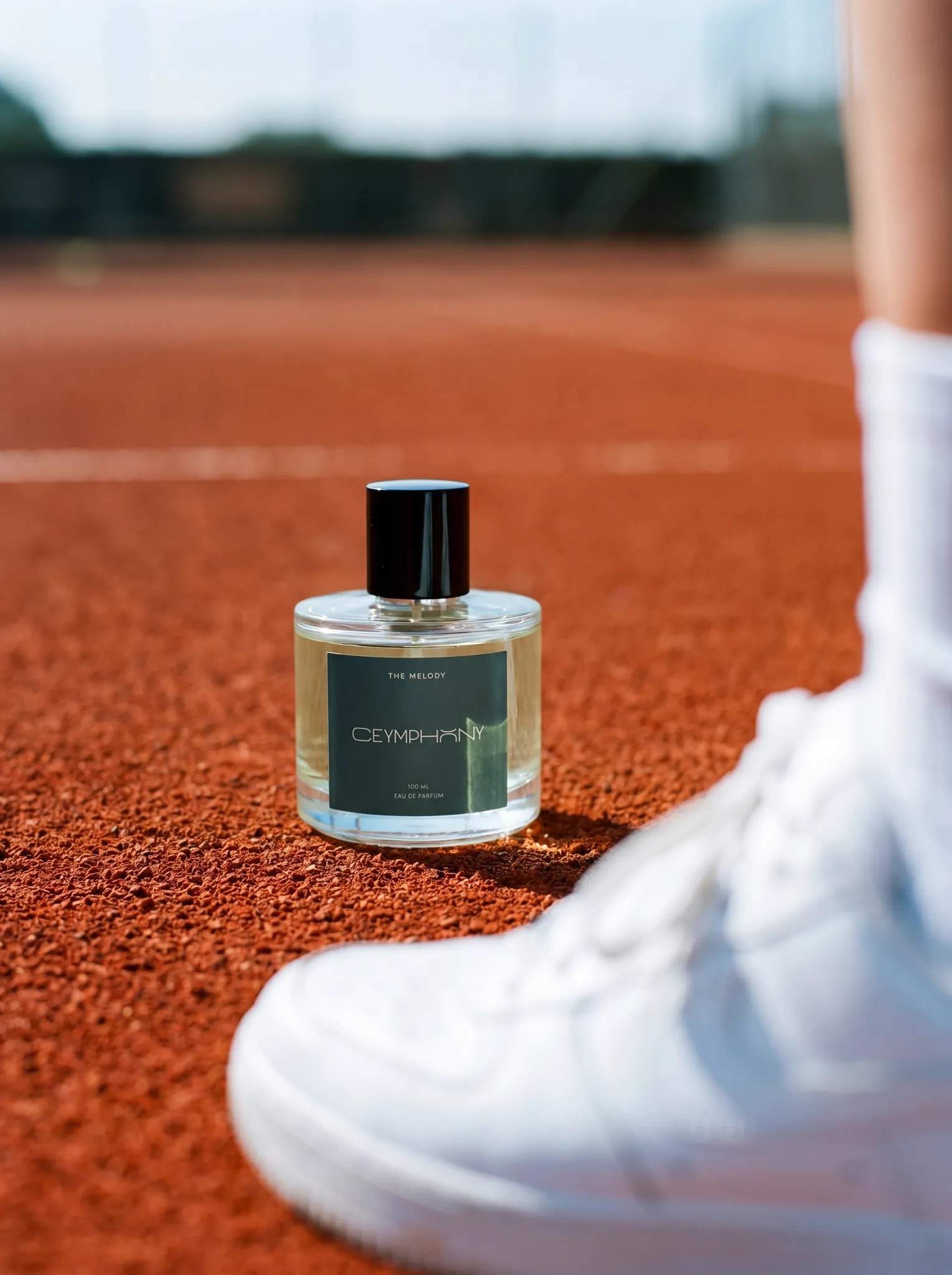 The Melody bottle on a sunlit red clay tennis court, a white sneaker just in frame.